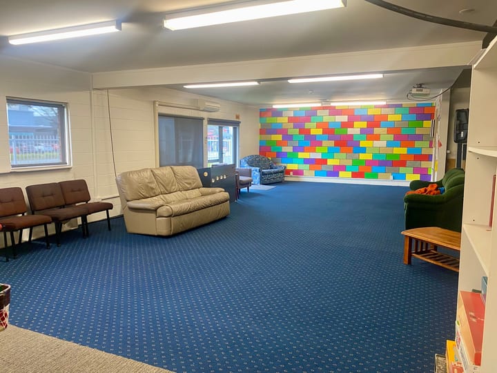 Carpeted room with sofas, chairs, and a colourful painted brick-pattern feature wall