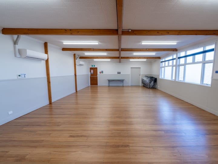 Empty hall with timber floor, exposed beams and natural light from high side windows