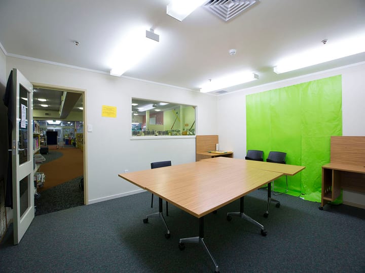 Meeting room with timber table, chairs, green feature wall, and window to library
