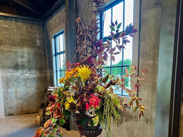 Large floral arrangement on a pedestal in a bare concrete-walled room with windows
