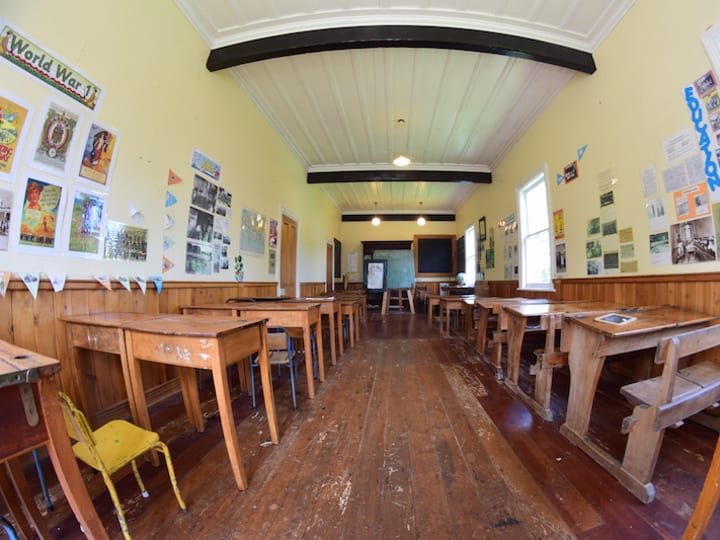 Heritage schoolroom with timber desks, blackboard, wooden wainscotting, and historical posters