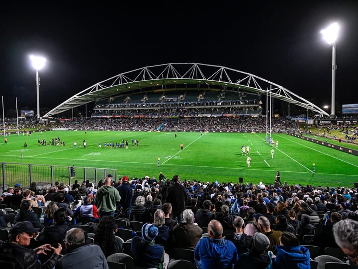 Stadium exterior lit up at night with large crowd in the stands and floodlights