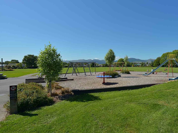 Open park with playground equipment, trees and mountain backdrop