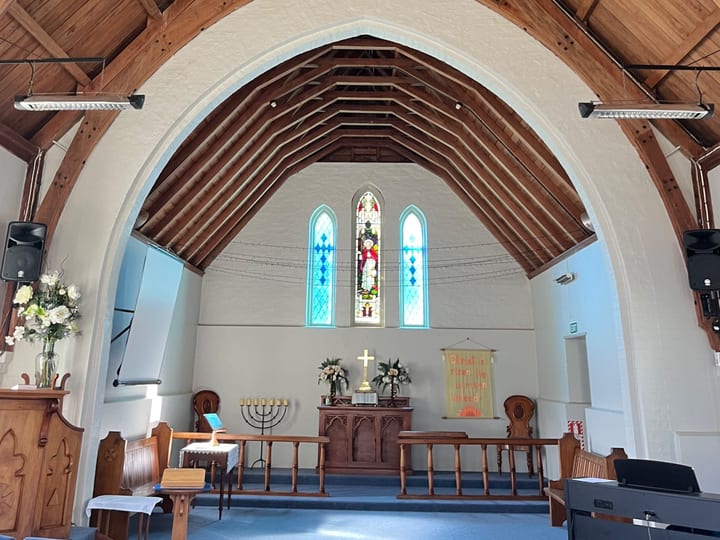 Church interior with timber vaulted ceiling, arched nave, stained glass windows, and altar