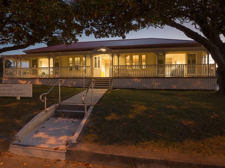 Illuminated heritage villa-style building at dusk with verandah and signage, trees framing