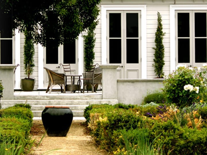 White heritage homestead with a formal parterre garden, columnar cypress trees and rose borders