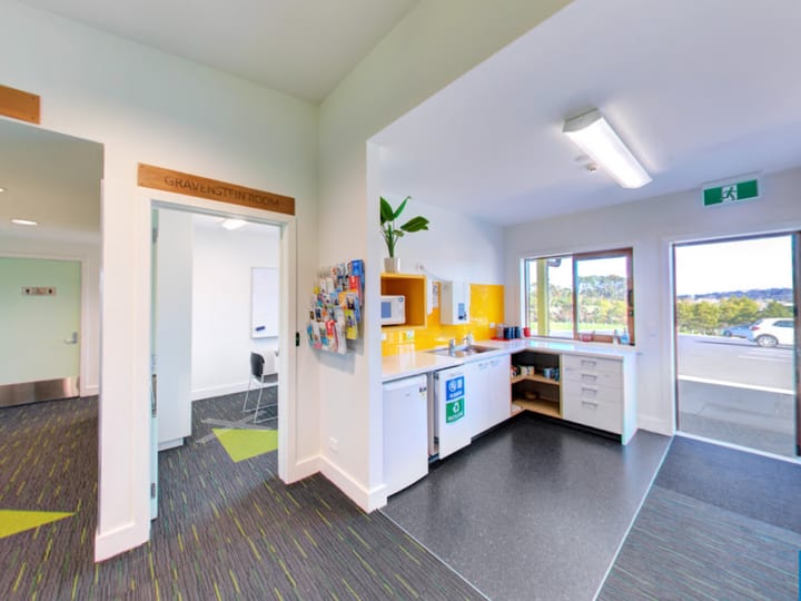 Foyer area with kitchenette, yellow accents, and view into meeting room