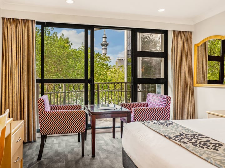 Hotel room with patterned armchairs, balcony doors and distant tower visible through trees