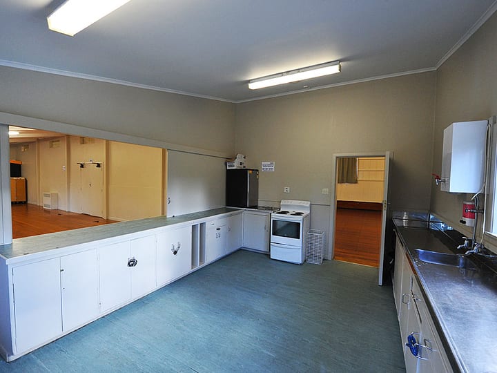 Supper kitchen with stove, white cabinetry and serving hatch to main hall