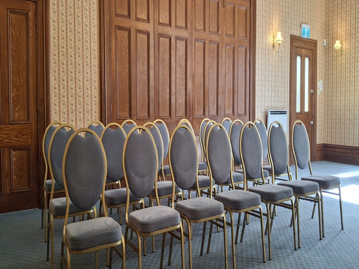 Rows of gold-framed chairs against panelled wall in Victorian function room