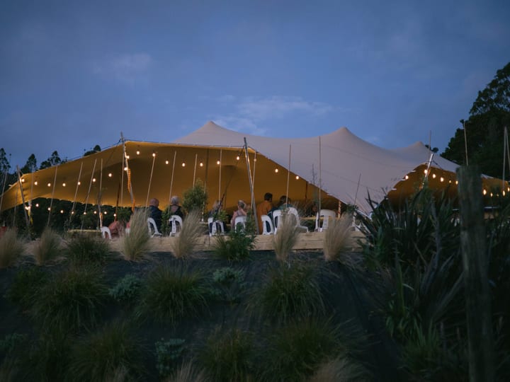 Illuminated stretch tent on hillside with guests seated at dusk