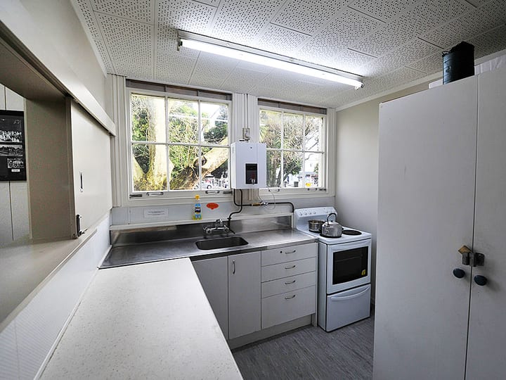 Hall kitchen with stainless bench, sink, stove and windows overlooking trees
