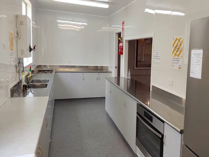 Plain white galley kitchen with stainless steel benchtops, white cabinetry, oven, and refrigerator
