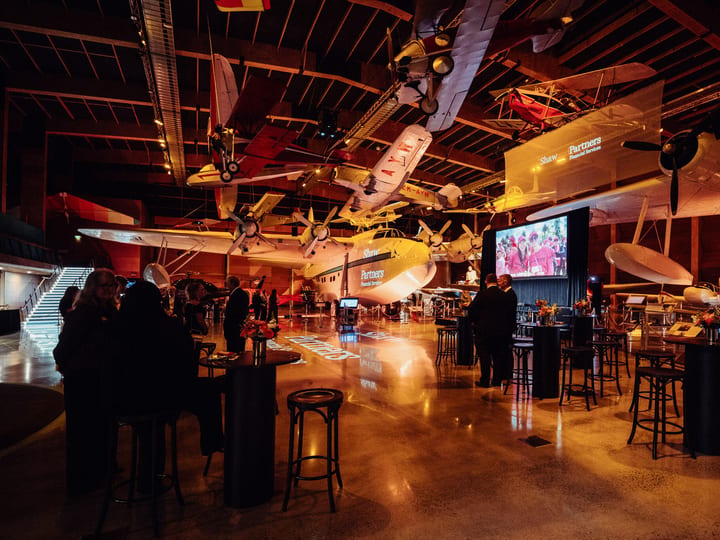 Event space inside a museum hall with vintage aircraft suspended overhead and cocktail tables