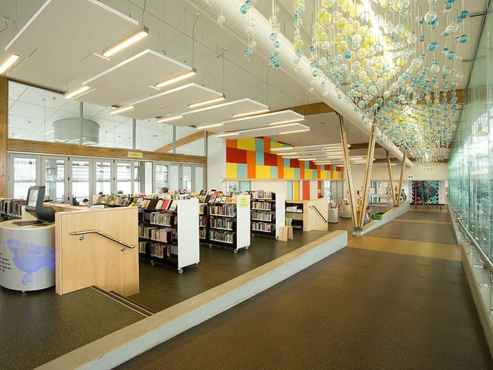 Open-plan library floor with timber shelving, colourful wall panels and glass pendant installation