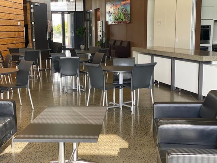 Open-plan function area with tables, chairs, kitchen servery, and artwork on wall
