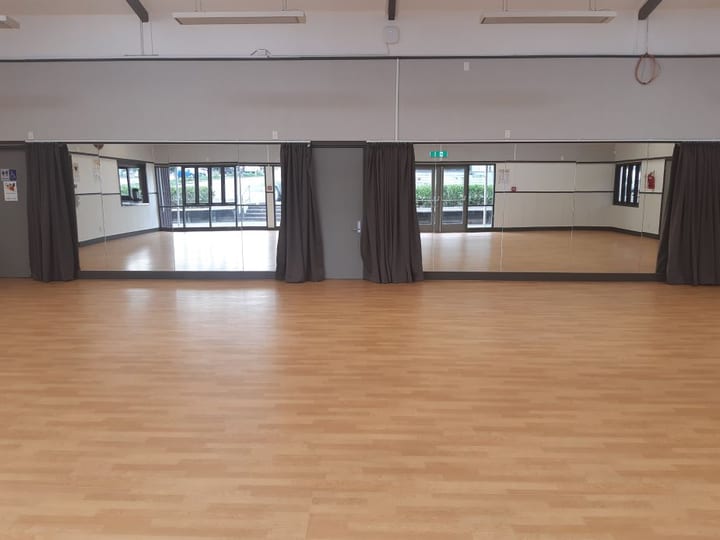 Empty timber-floored hall room with mirror wall and curtain