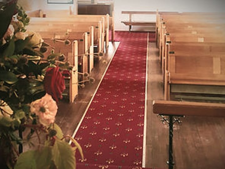 Church interior with timber pews, red carpet aisle and flower arrangements