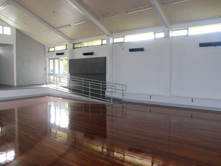 Hall with polished timber floor, vaulted ceiling, and low raised platform with storage cabinets