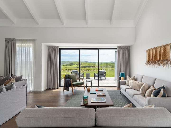 Light-filled lounge with grey sofas, large sliding doors opening to green hillside, woven wall panel