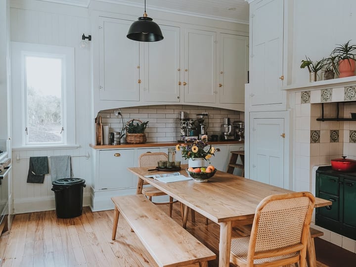 Country kitchen with timber table, bench seating, white cabinetry and dark range cooker