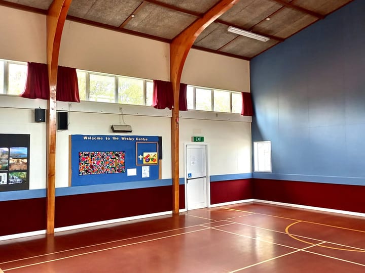 Multi-use hall interior with timber-arch portal, blue and red painted walls, and court markings