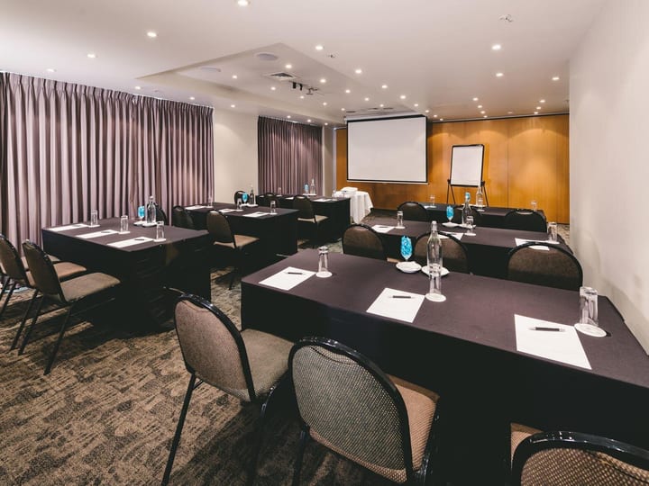 Conference room with dark tablecloth tables, projection screen and drapes