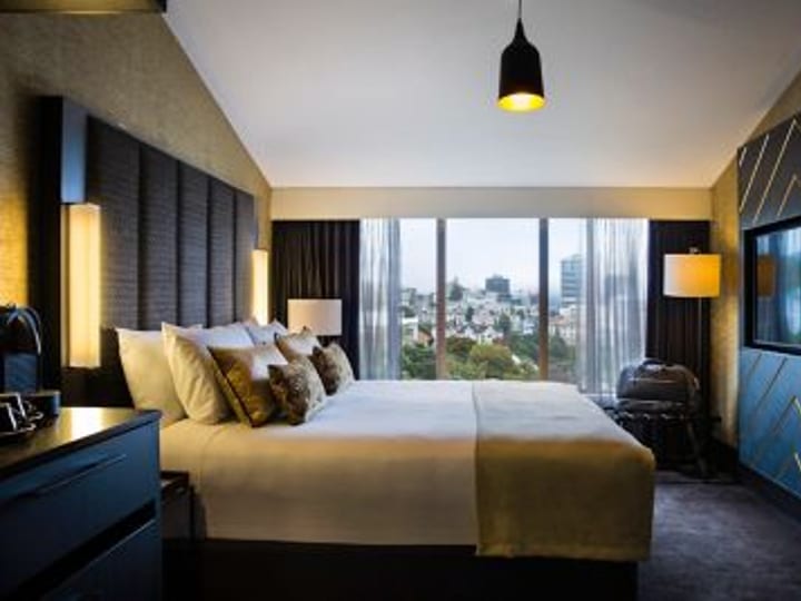 Hotel room with large bed, dark panelled headboard, and city-view windows