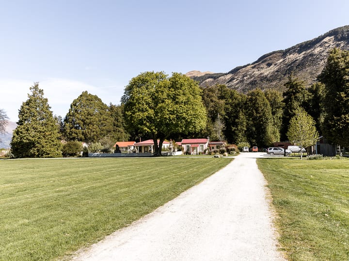 Gravel driveway leading to red-roofed cottages with mountains and trees in the background