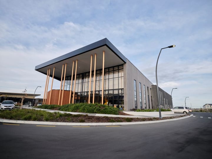 Contemporary building with glazed curtain wall, dark metal upper cladding, and bronze columns at entrance