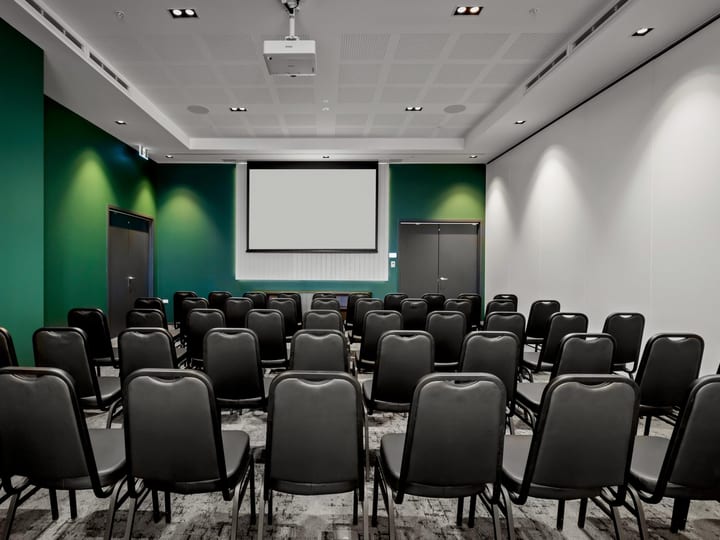 Dark green-walled function room with theatre-style rows of black chairs and a projection screen