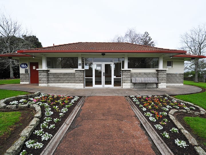 Front facade of low hall building with tiled roof, garden bed and entrance path