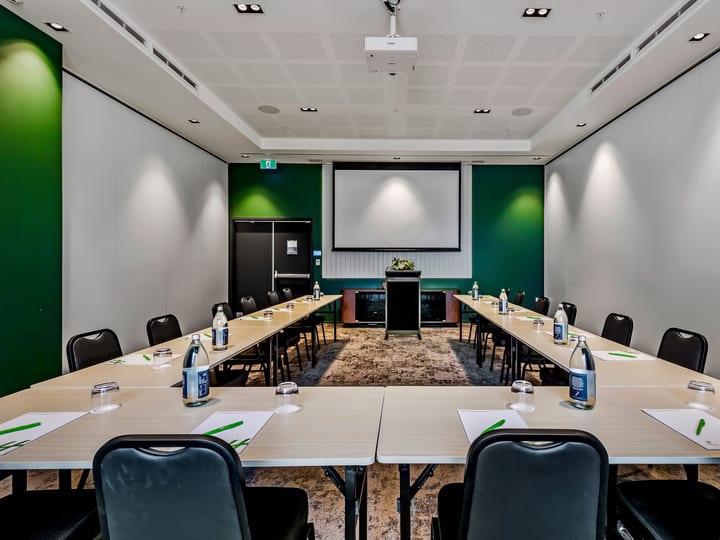 Meeting room in U-shape layout with green accent wall, projection screen, and patterned carpet