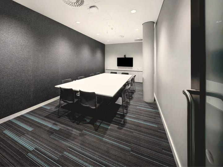 Compact meeting room with white table, black chairs, wall-mounted screen and dark acoustic panelling