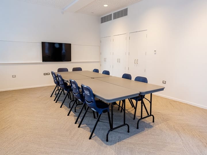 Small meeting room with wall-mounted screen, whiteboard, boardroom table and blue chairs