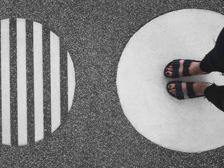 Overhead view of feet in sandals standing on painted circle markings on asphalt