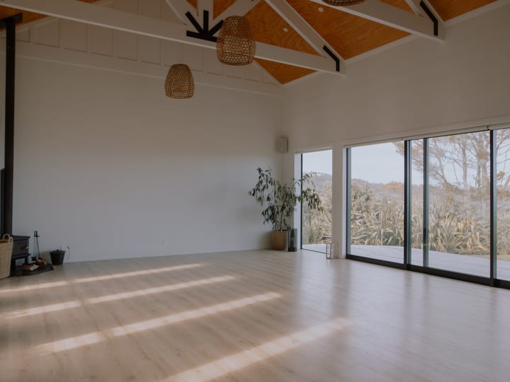 Light-filled open space with vaulted timber ceiling, pale floorboards, wood burner, and sliding glass doors