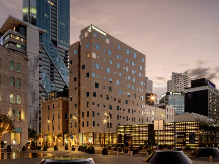 Pale brick multi-storey building with irregular window openings, city skyline at dusk