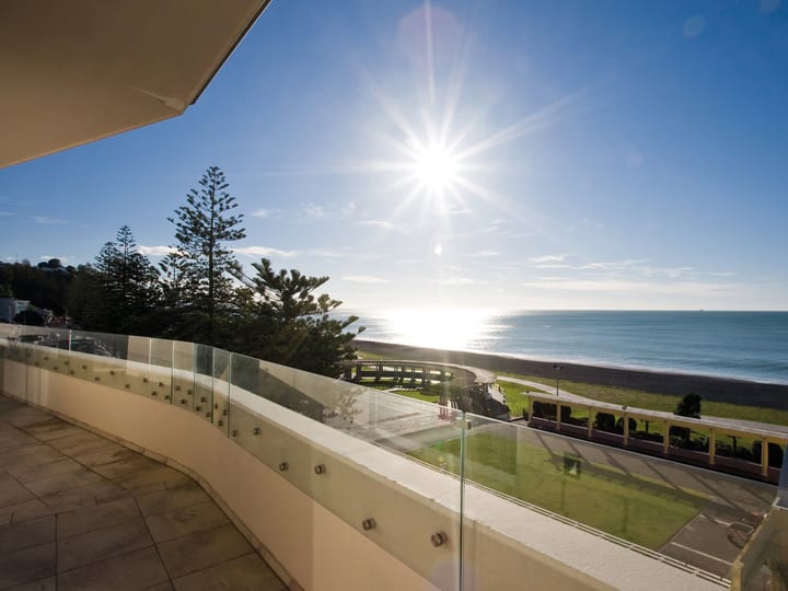 White rendered building balcony with glass balustrade overlooking beach, sea and pine trees