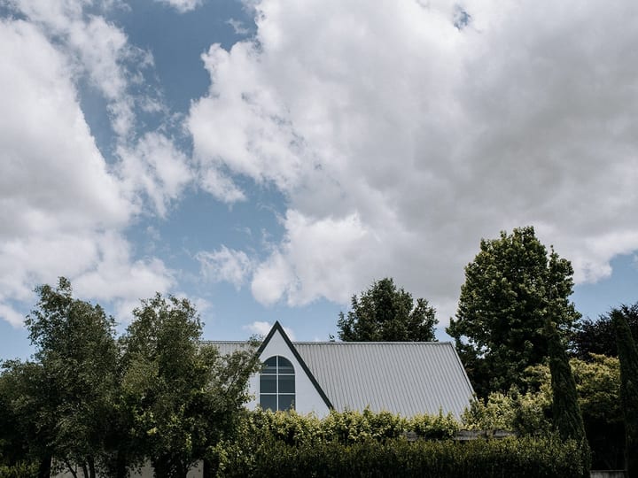 White metal-roofed building partially visible above trees against a cloudy sky