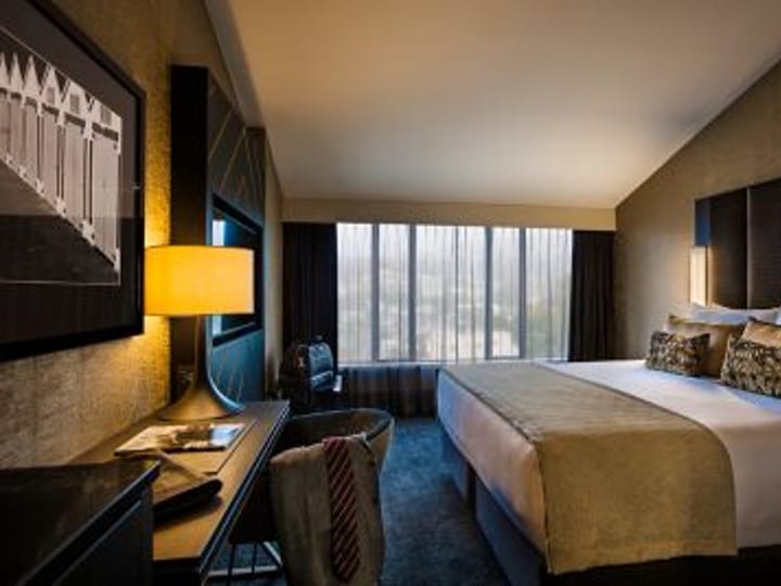 Dark-toned hotel room with large bed, desk, and floor-to-ceiling windows