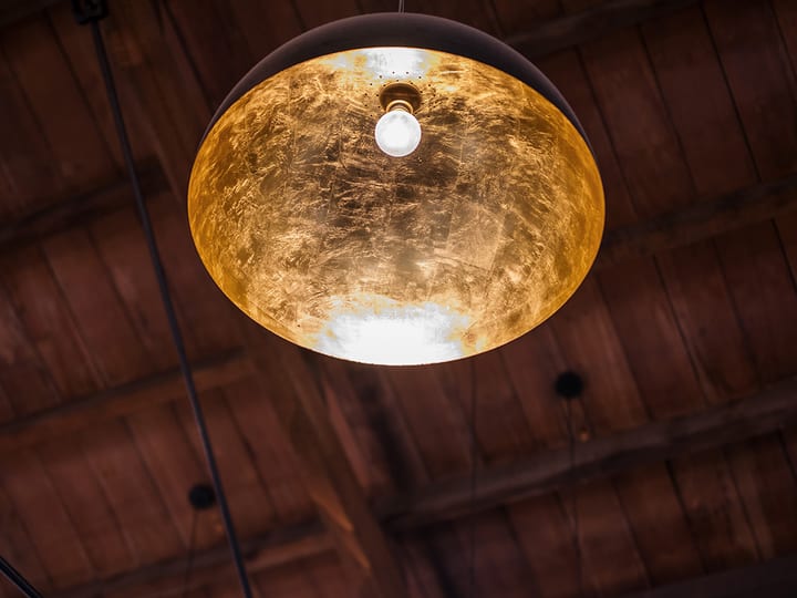 Gold pendant lamp hanging from dark timber rafter ceiling