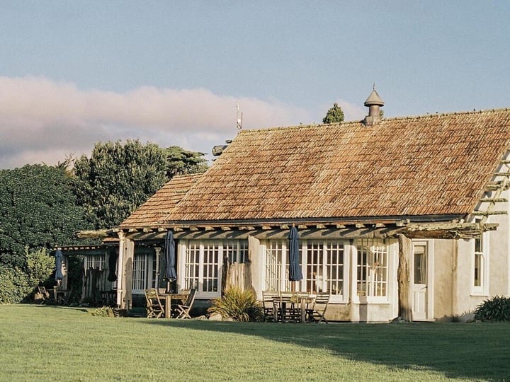 Timber and plaster lodge building viewed from lawn with outdoor dining on verandah
