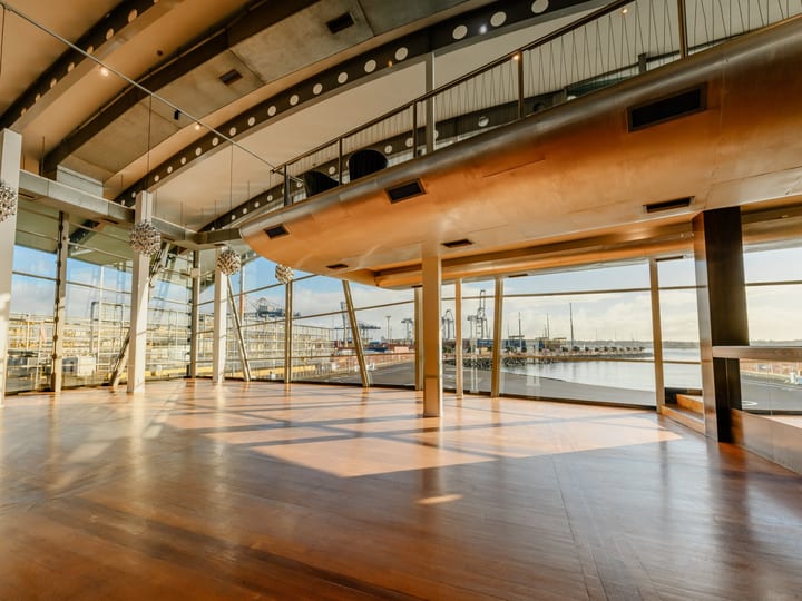 Double-height curved event space with floor-to-ceiling glazing and harbour views at low sun