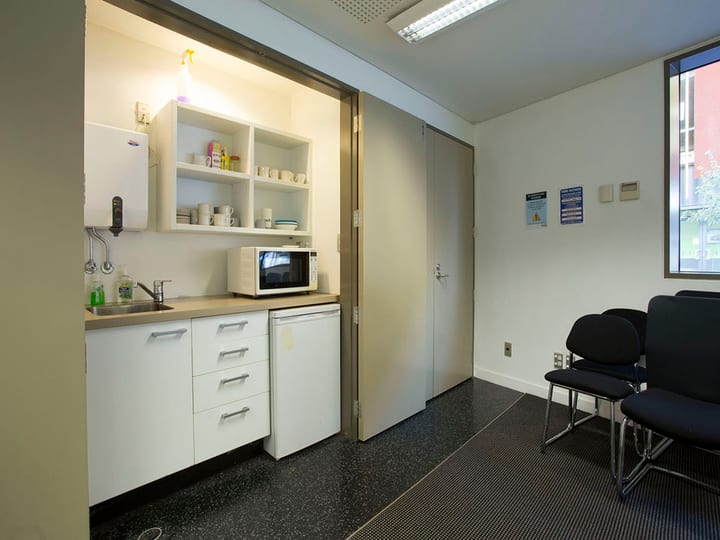 Small kitchenette alcove with microwave and sink beside waiting chairs