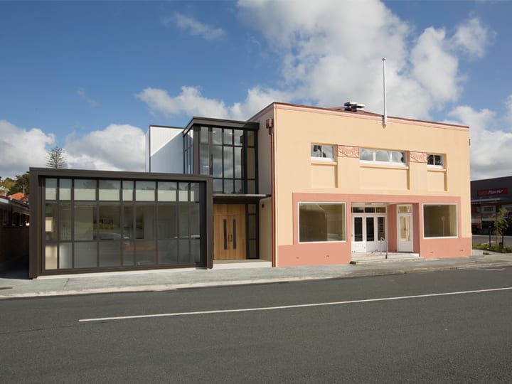 Salmon-rendered two-storey hall with glass extension and dark-framed shopfront, street view