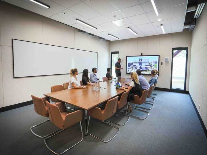 Meeting room with people around a table, a large screen, and a whiteboard