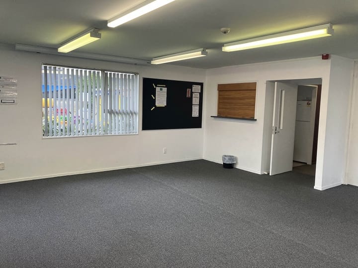 Carpeted room with noticeboard, window with vertical blinds and opening to adjoining space