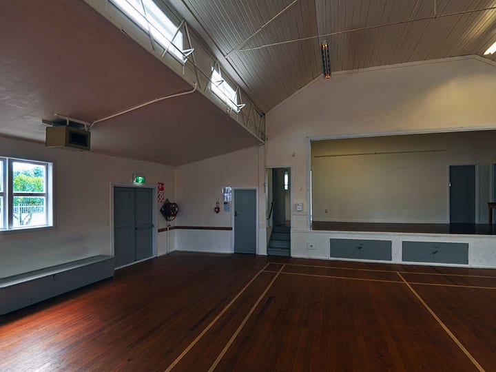 Empty hall interior with polished timber floor, raised platform, and side stage area