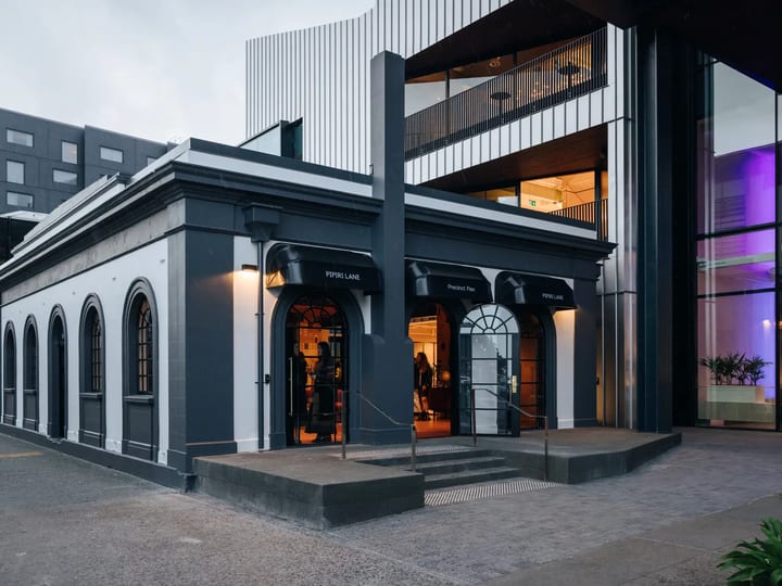 Dark rendered heritage building with arched shopfront openings and modern upper addition, street entrance at dusk